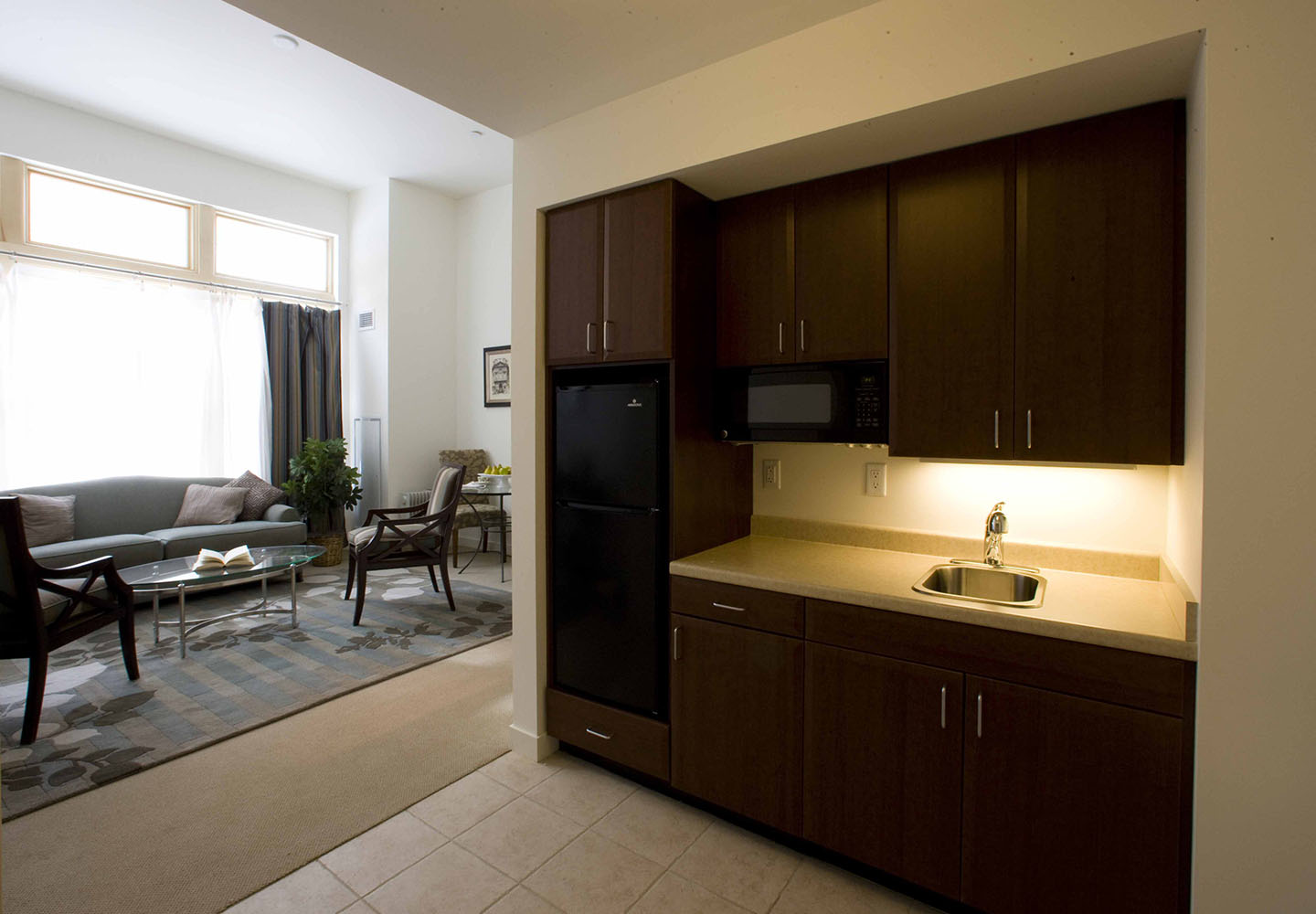 A kitchenette opens to a sunny living room in an assisted living apartment at NewBridge on the Charles.