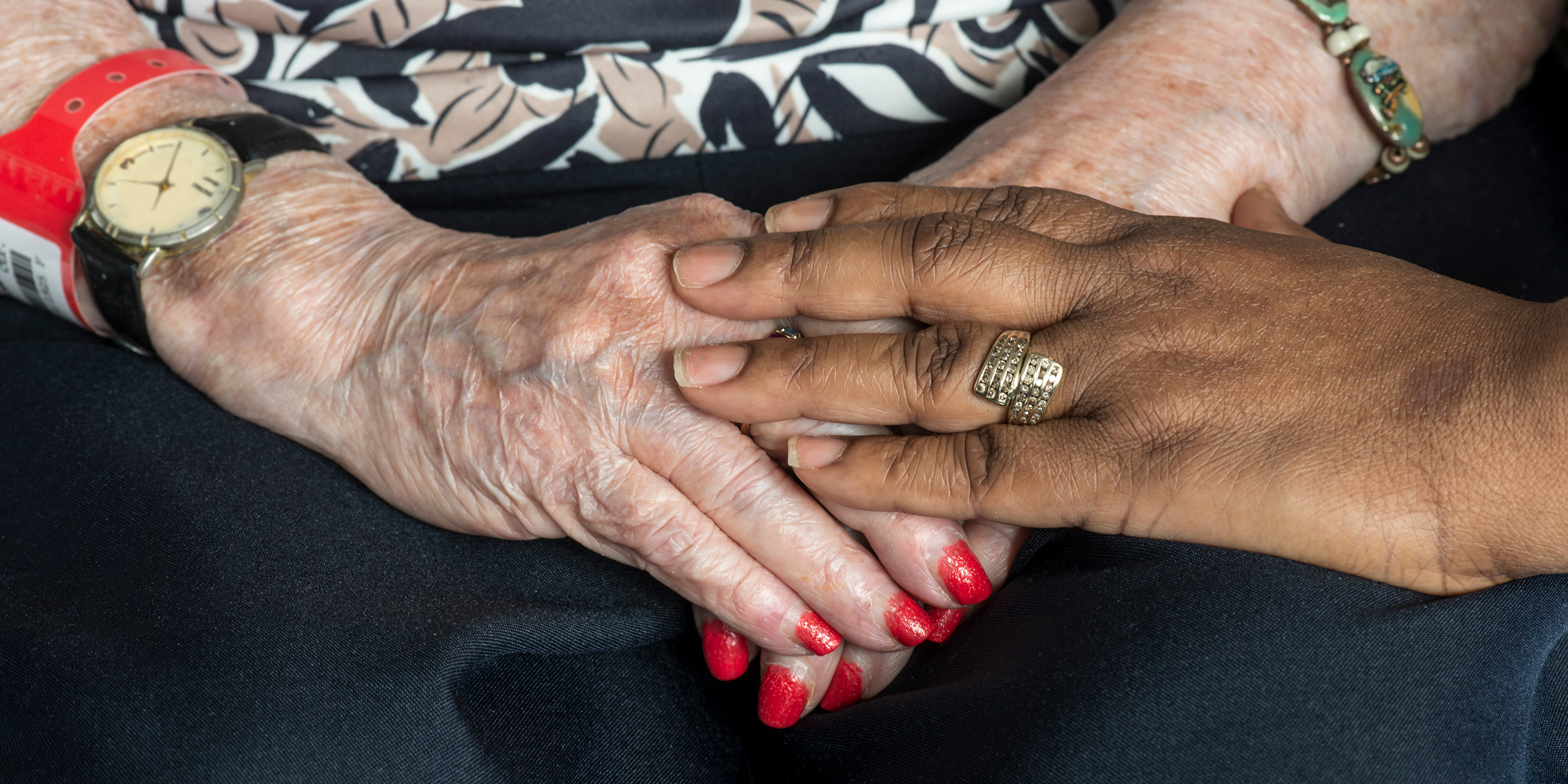 A close up of two women's hands - one woman has her hands in her lap while the other woman pats her hand.