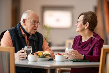 Two seniors sitting at a meal and holding glasses of water