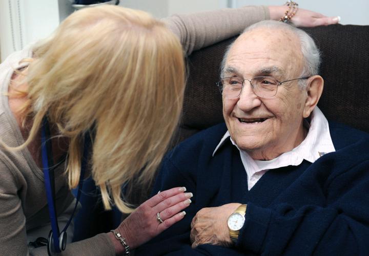 Older man seated and smiling as he speaks with a Hebrew SeniorLife hospice nurse.