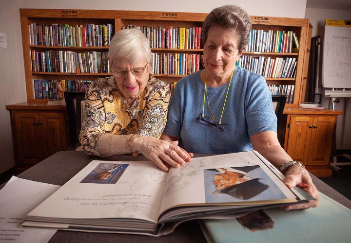 Two older women look through a large book in the library.