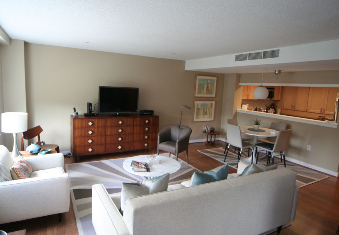 Living room with couch, sitting chair and coffee table with a kitchen in the background.