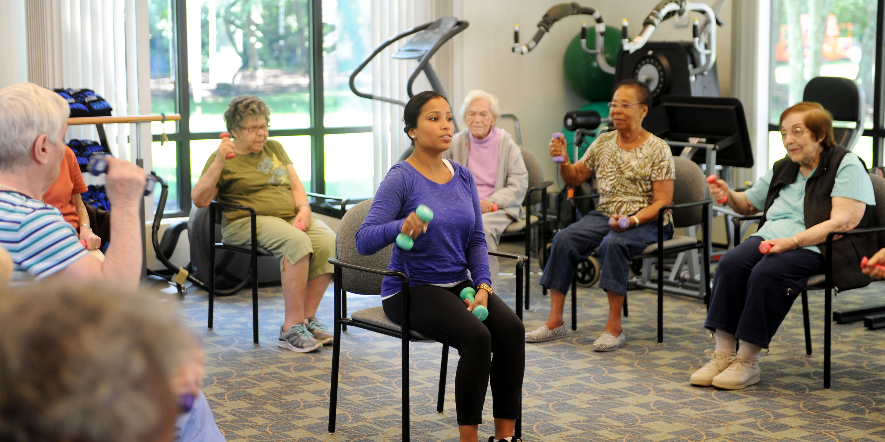 A female fitness instructor leads a group of seniors in a group fitness class involving weights. 