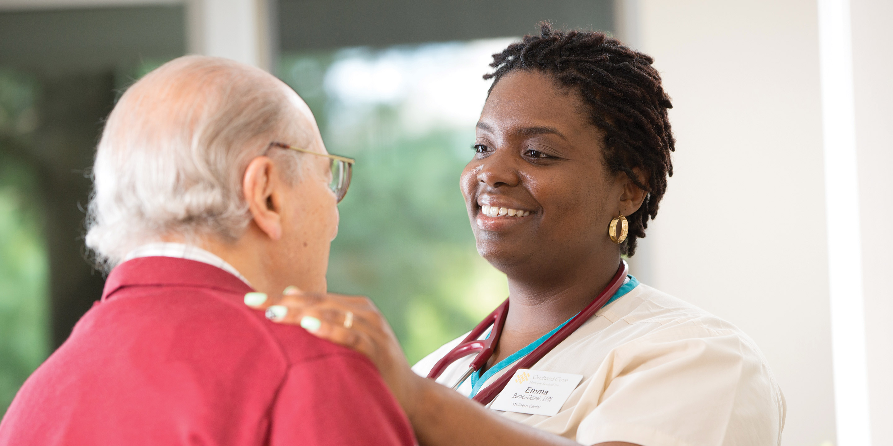 A young woman caregiver places her hands on an older man's shoulder. 