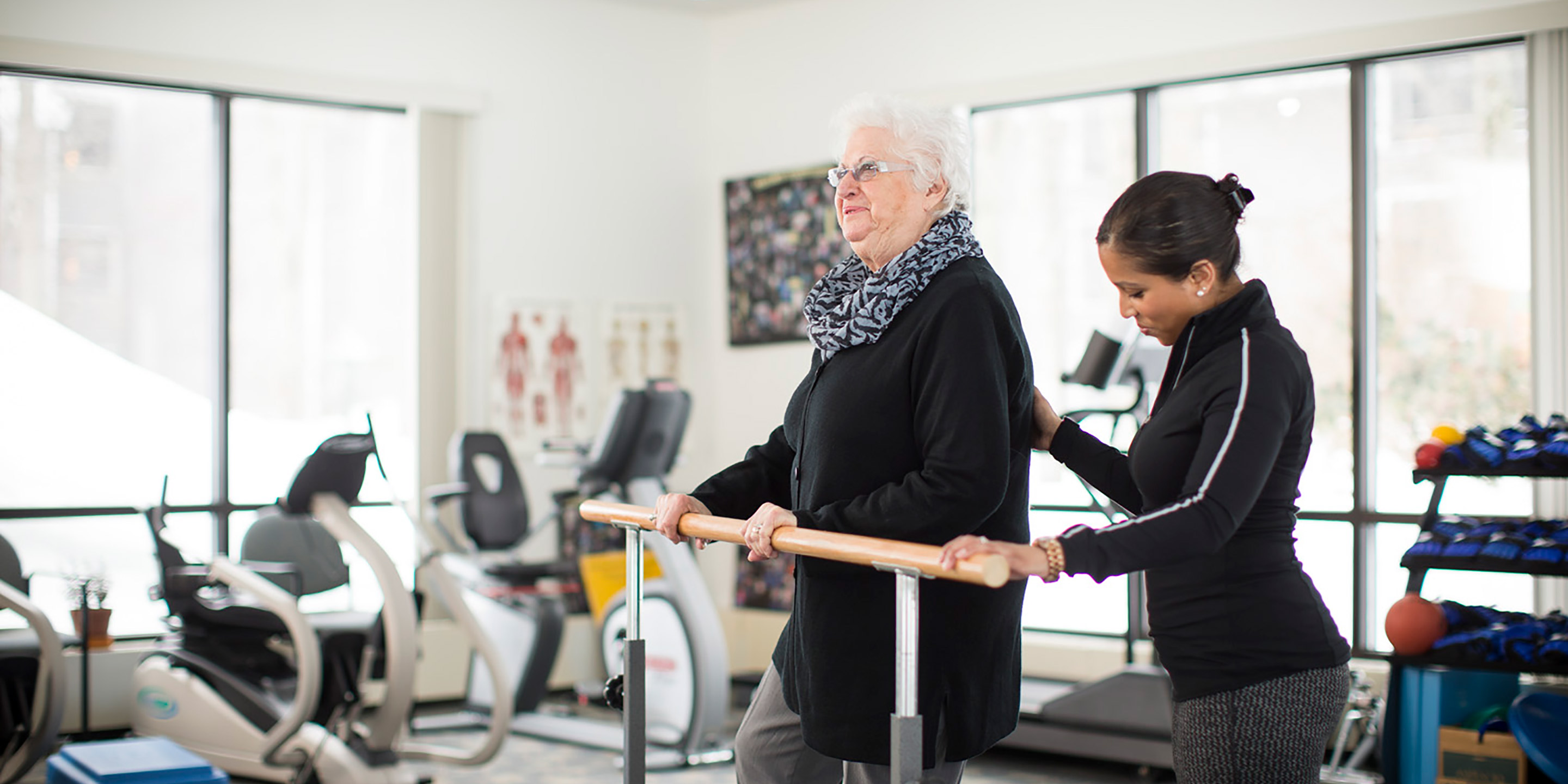 An older woman works out in a rehabilitation gym with a trainer