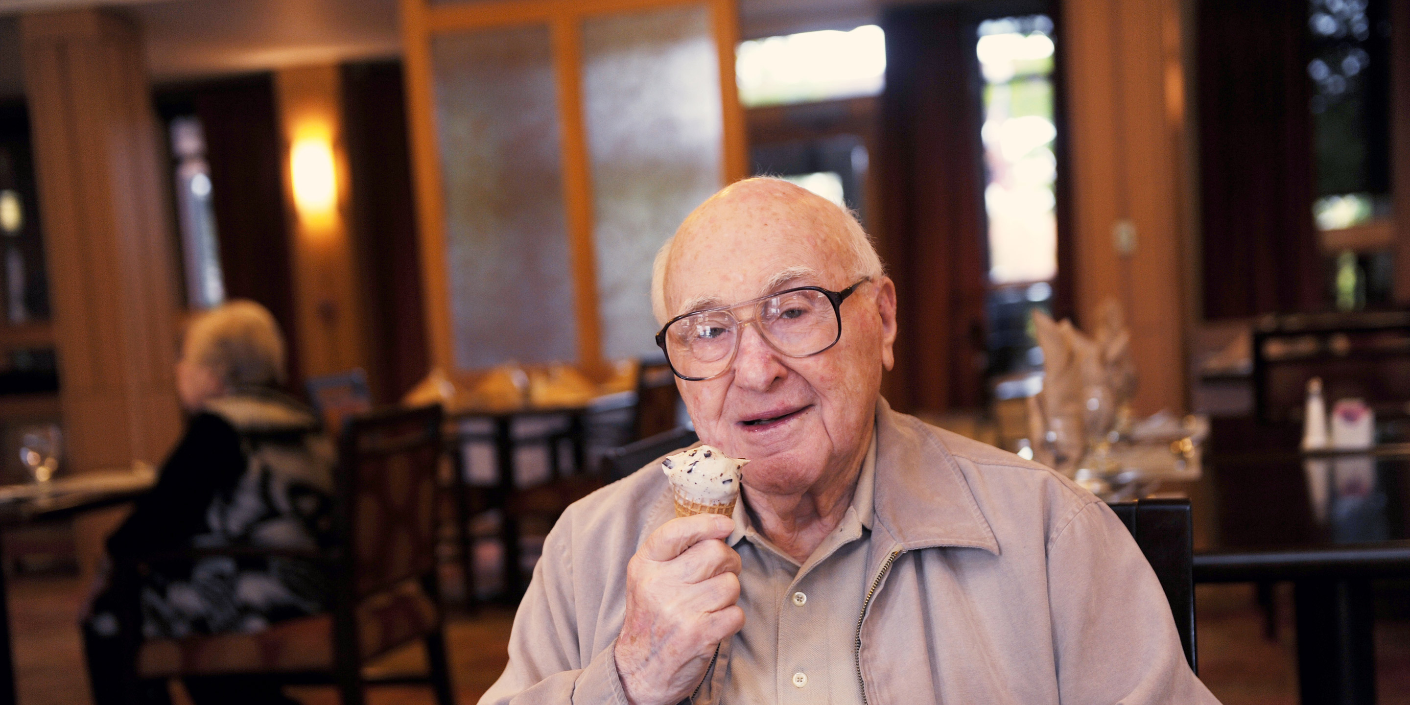 A man with glasses smiles while holding an ice cream cone in a dining room