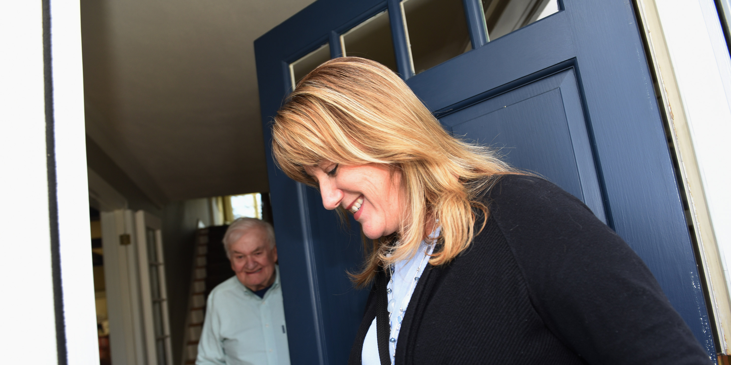 At the doorstep of his house, a nurse from Hebrew SeniorLife Home Health greets older man using a walker