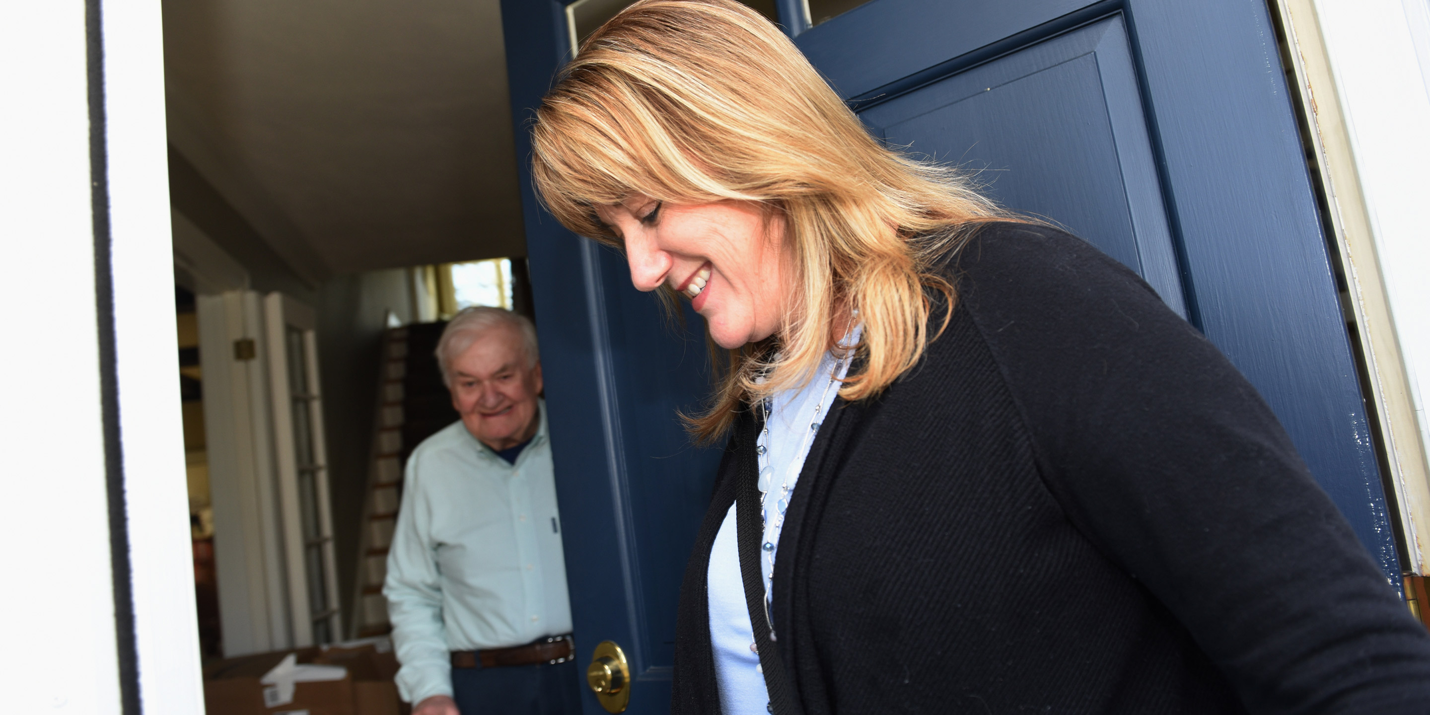 At the doorstep of his house, a nurse from Hebrew SeniorLife Home Health greets older man using a walker