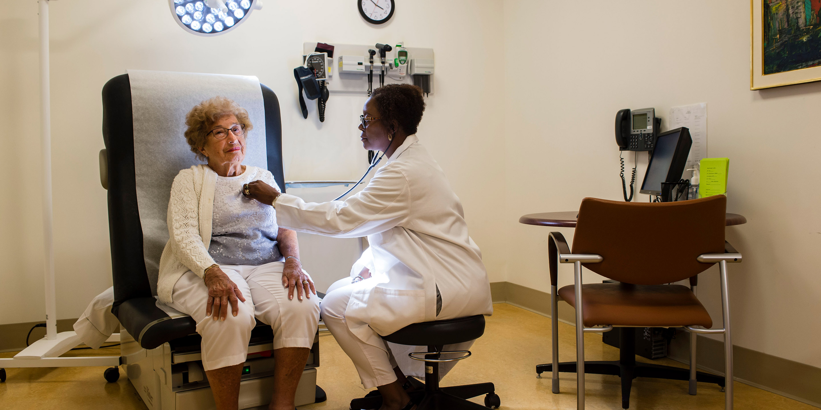 A Hebrew SeniorLife doctor listens to the heartbeat of a community resident in an exam room