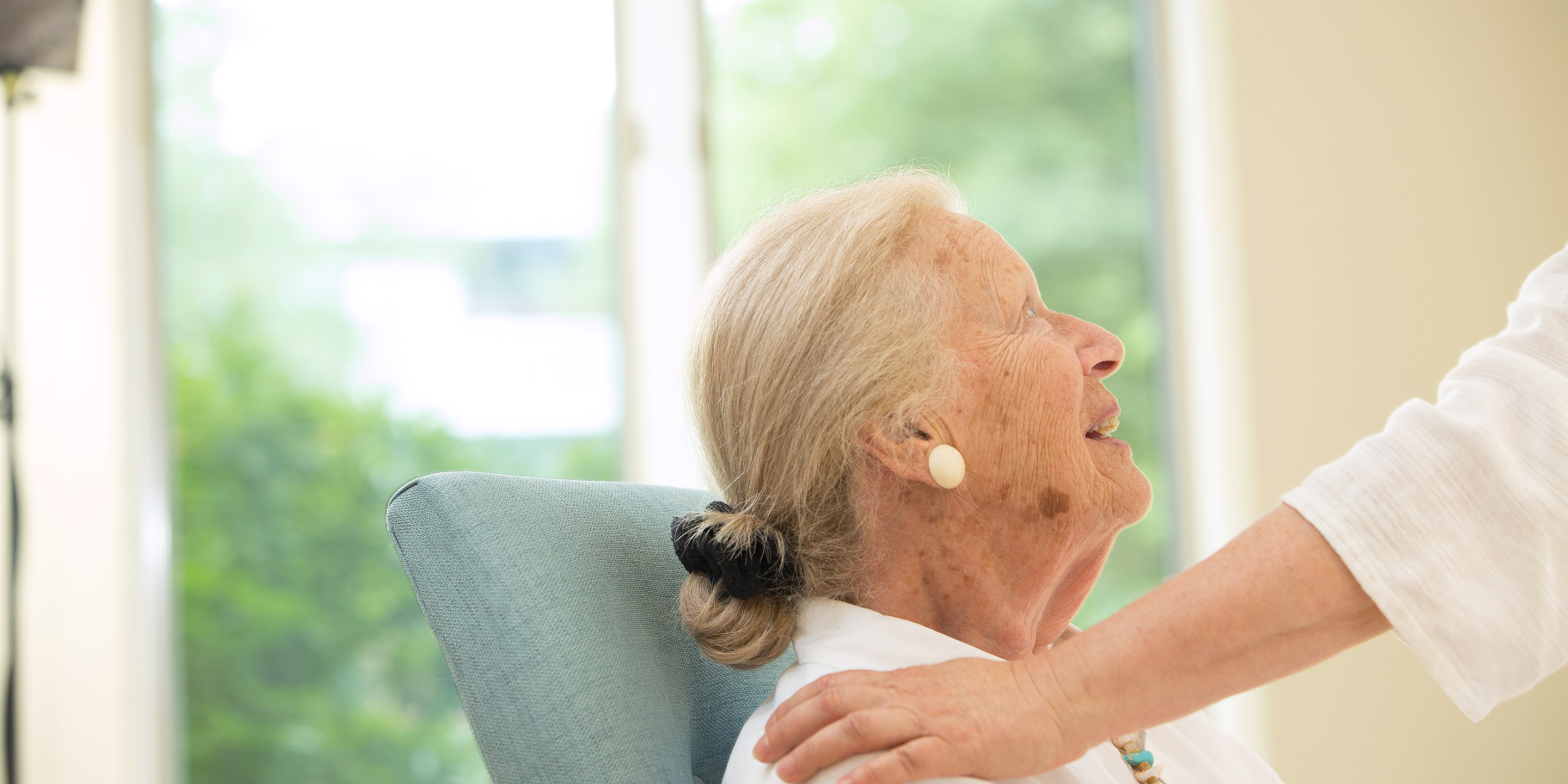 A female resident looks up and smiles as someone pats her shoulder 