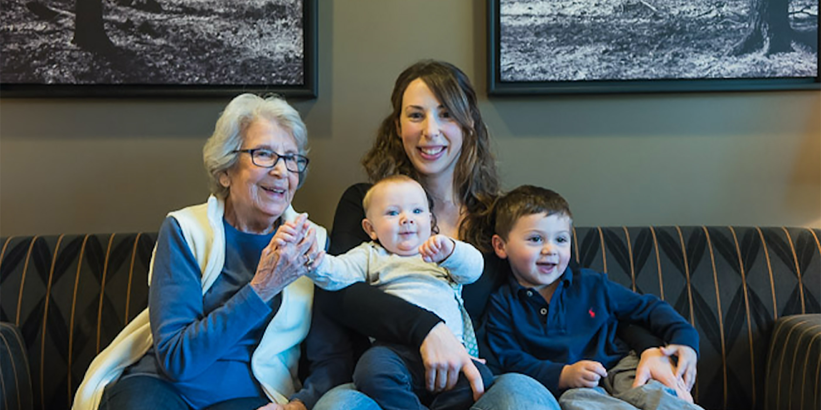 A elder woman sits with a younger woman and two children on a couch