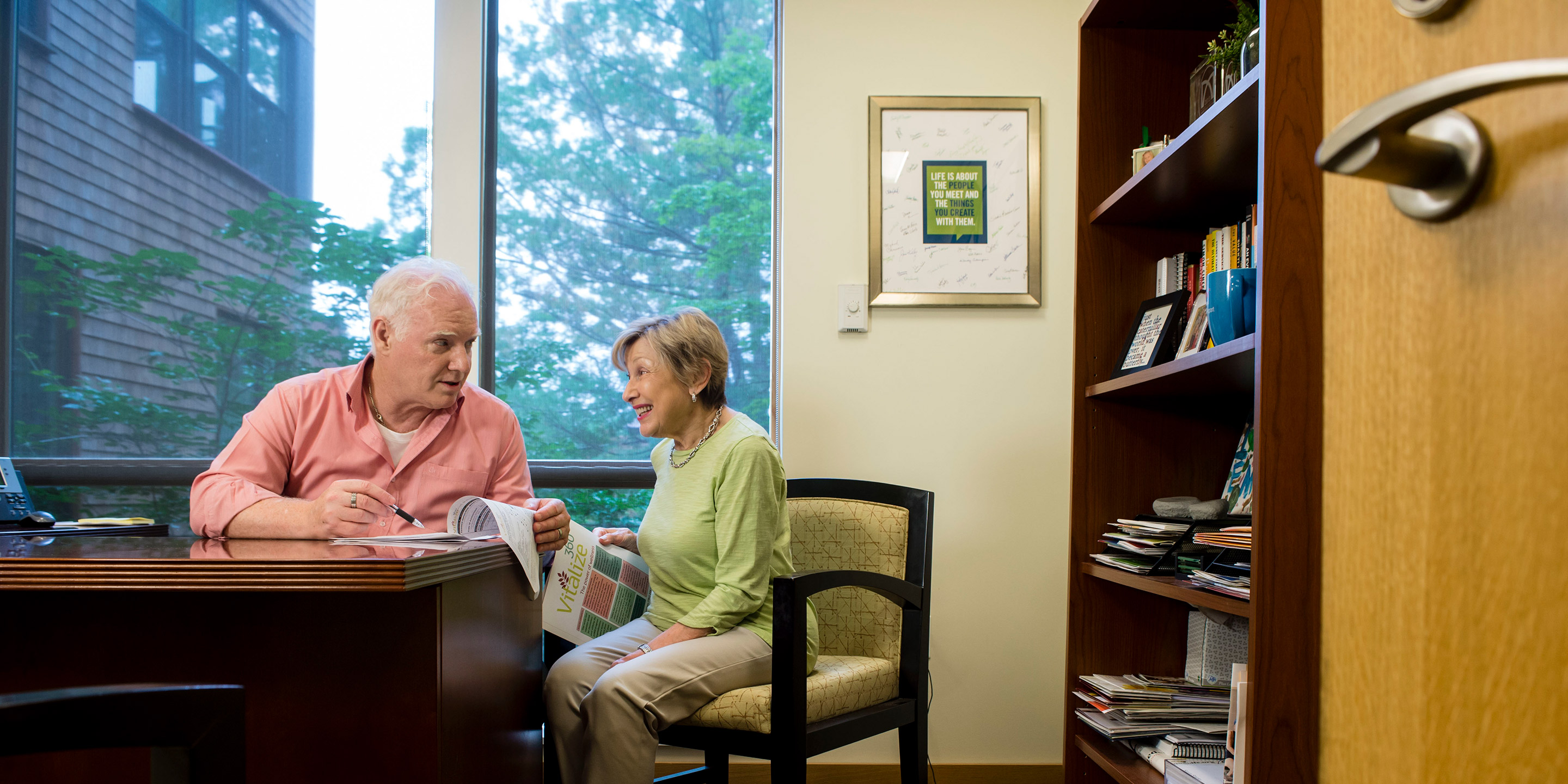 A male and female sit together in a library to fill out paperwork for Vitalize 360
