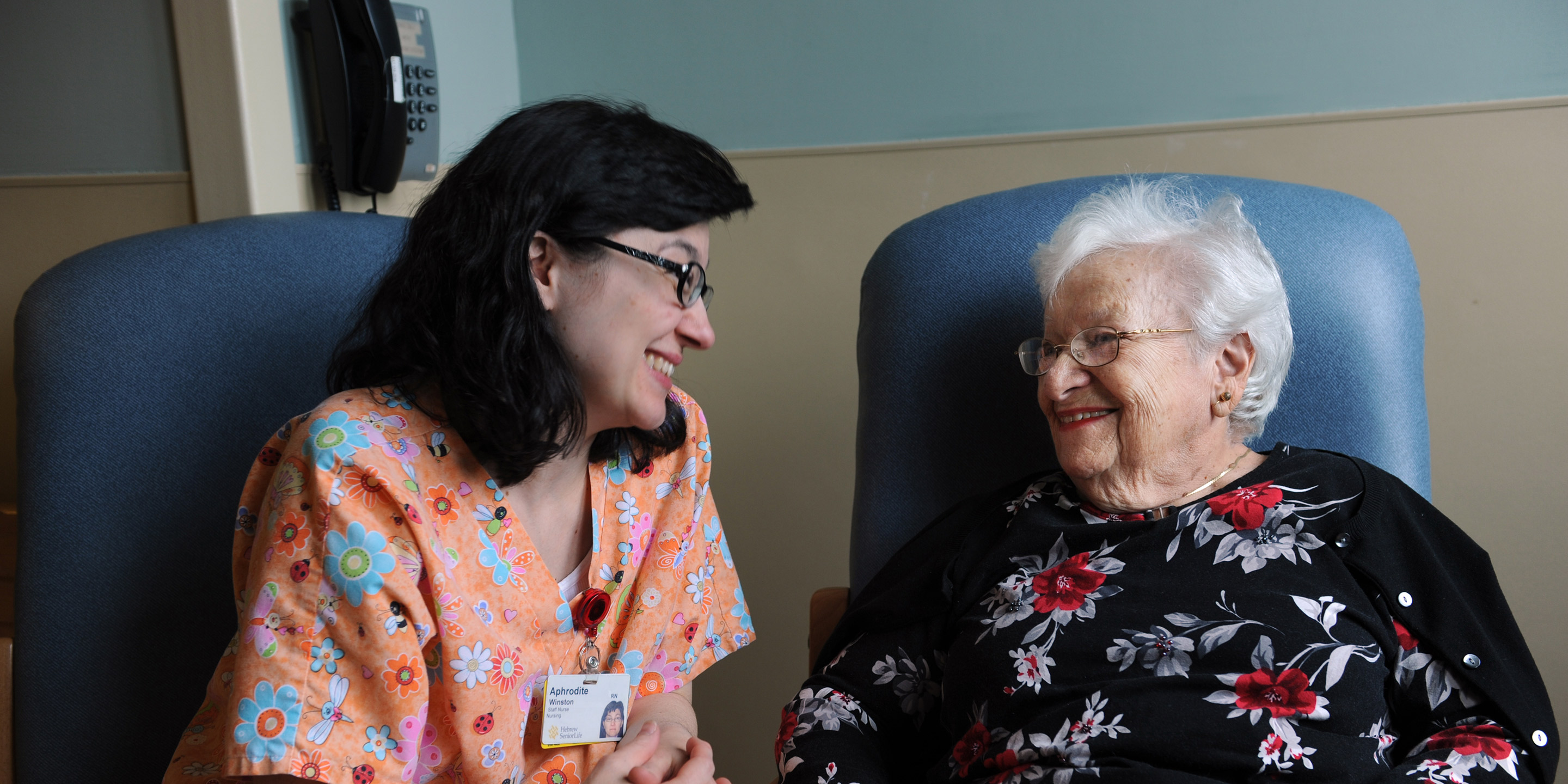 A smiling caregiver sits and talks with a senior 