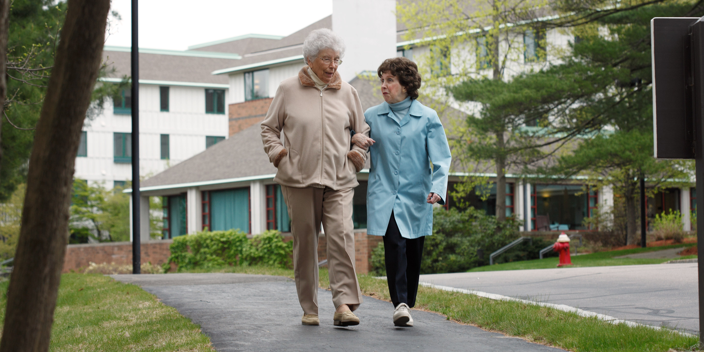 Two senior female friends walk together arm in arm