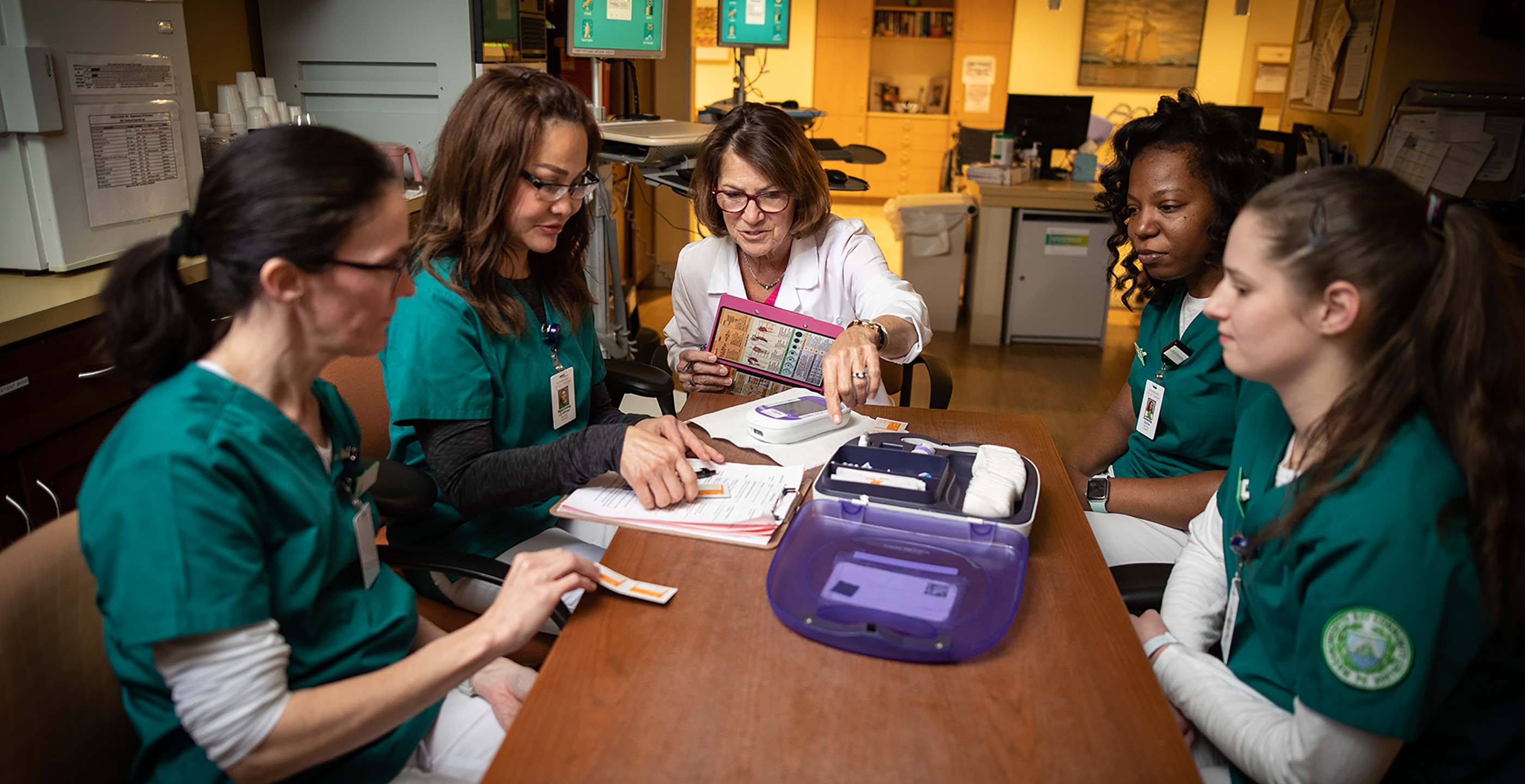 A group of nursing students sit around a table to learn from a Hebrew SeniorLife employee 