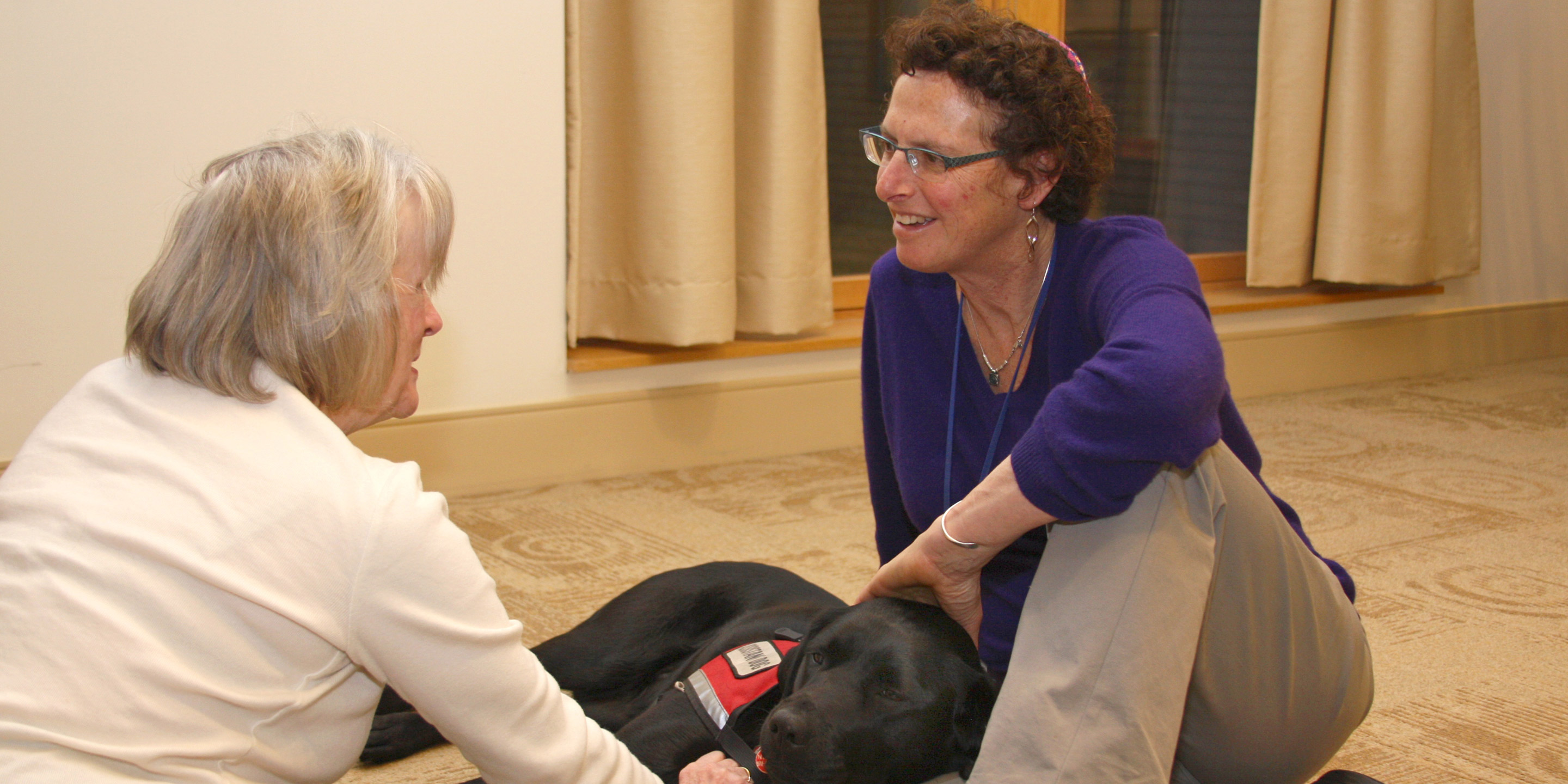 Rabbi Karen Landy and Tamari, her ministry service dog, sit on the floor with an elder woman