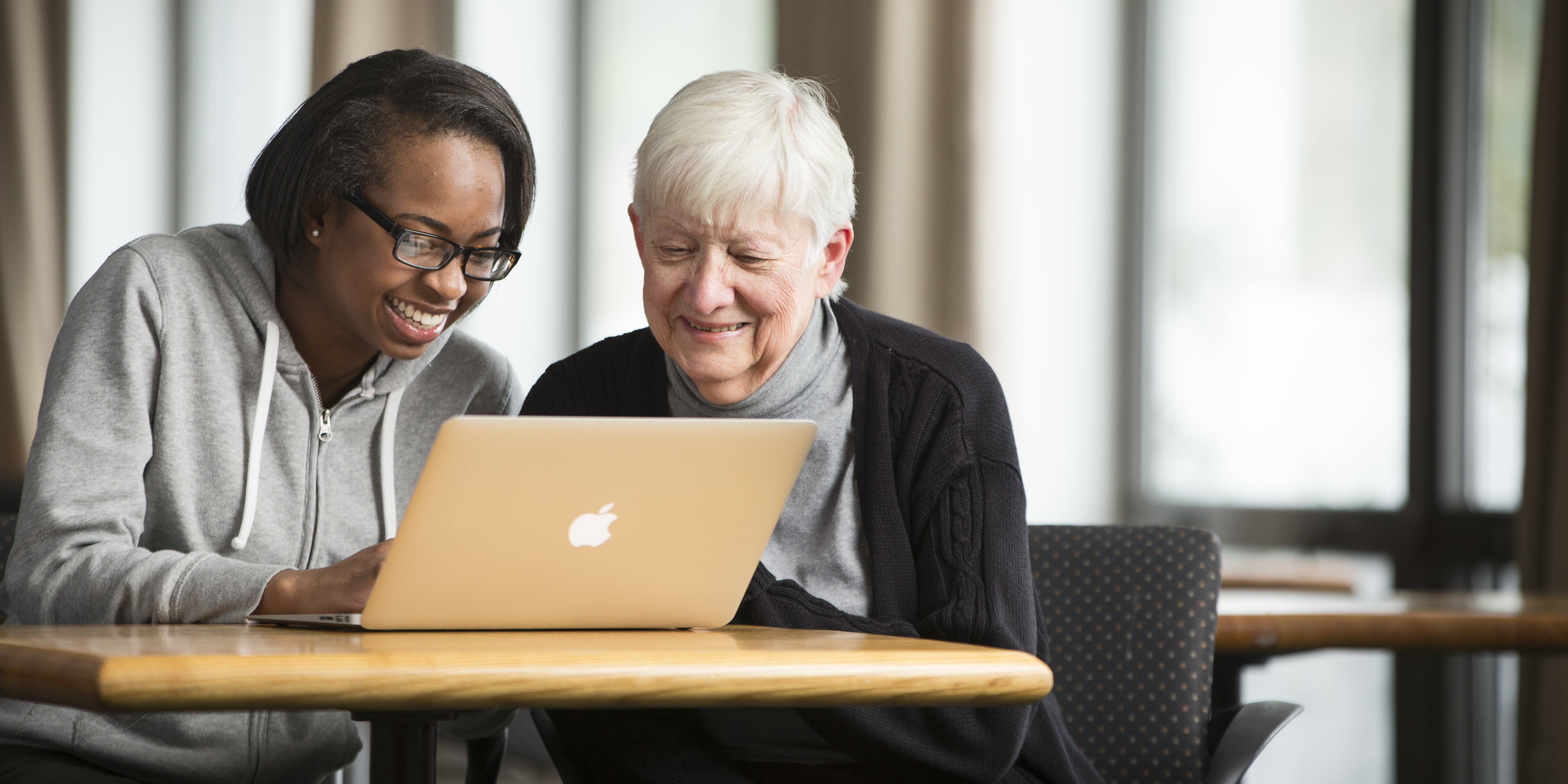 two women sit at table and look at computer 