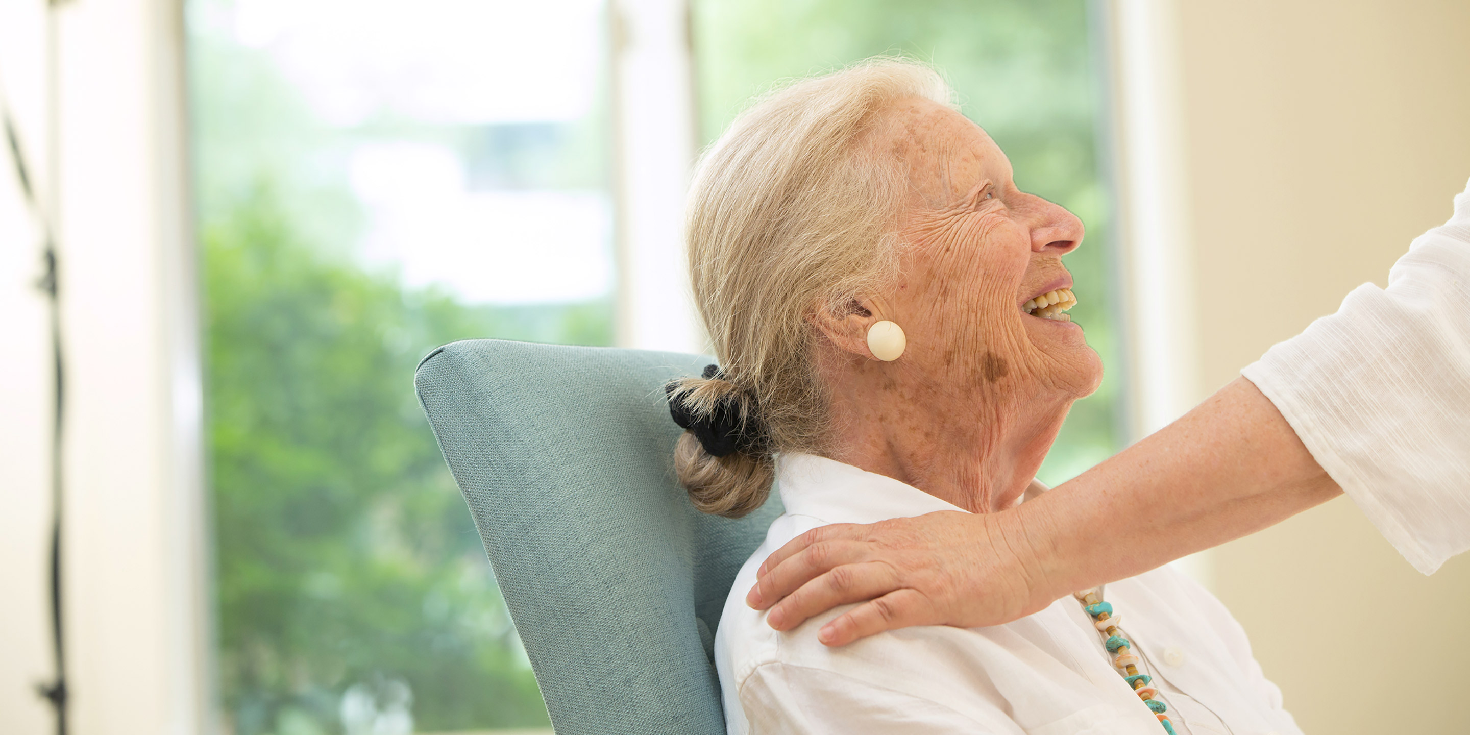 A female resident looks up and smiles as someone pats her shoulder 