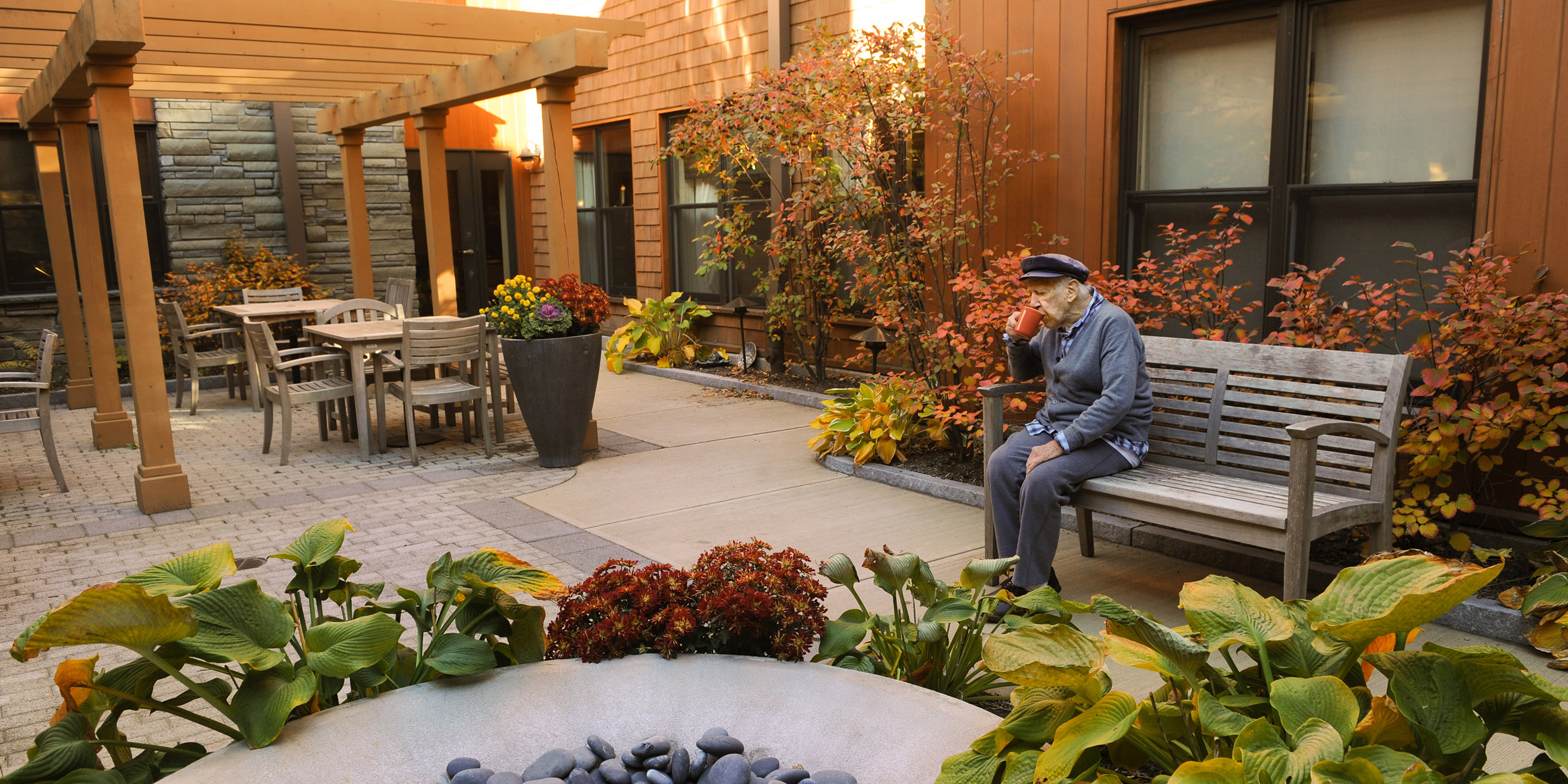 A resident sits outside on a bench and sips his coffee. 