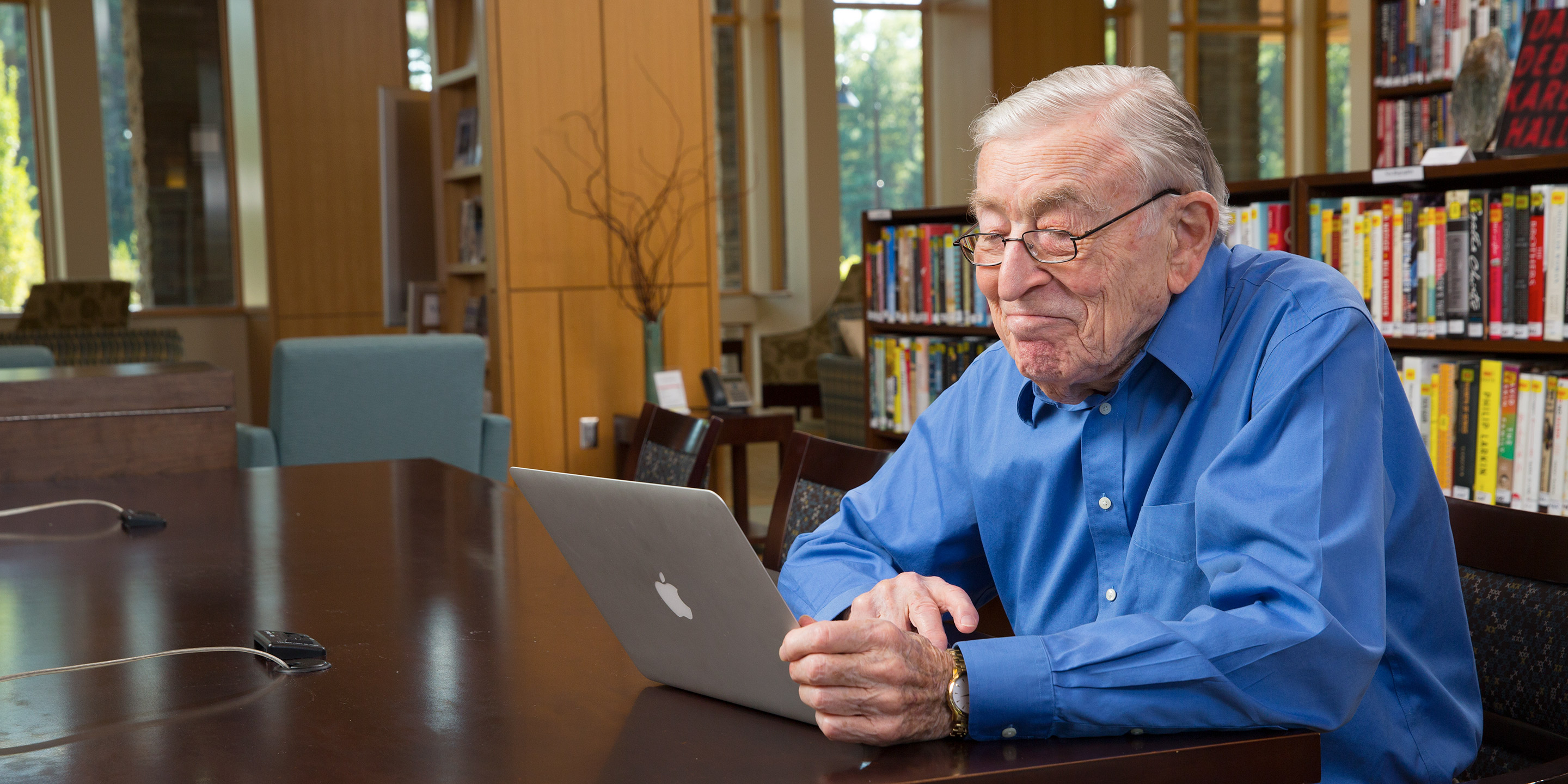 An older man smiles while using a laptop.