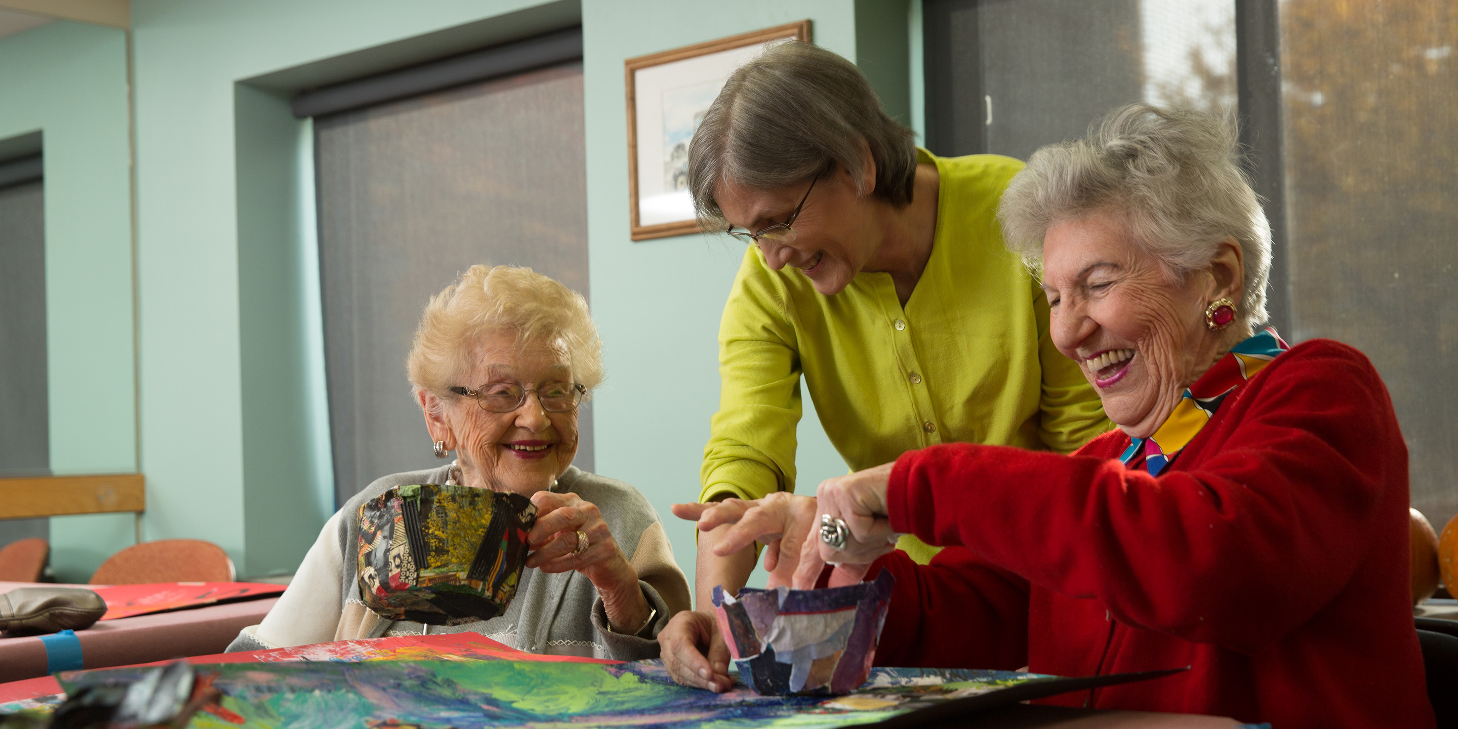 Art instructor showing two smiling women how to make colorful paper mache bowls