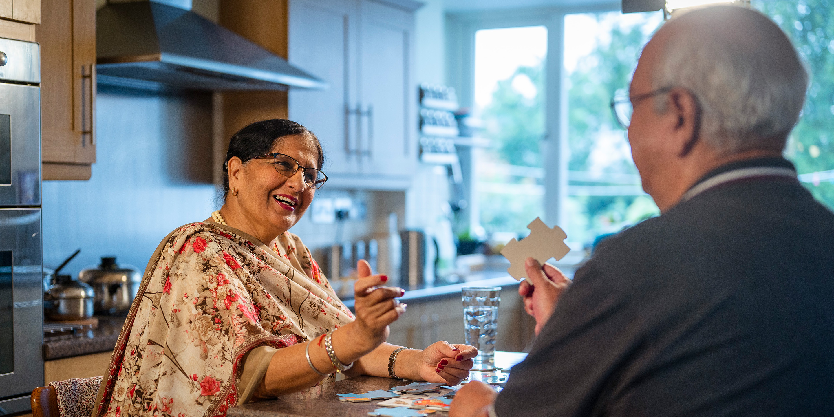 Older couple sitting in kitchen putting together a puzzle.