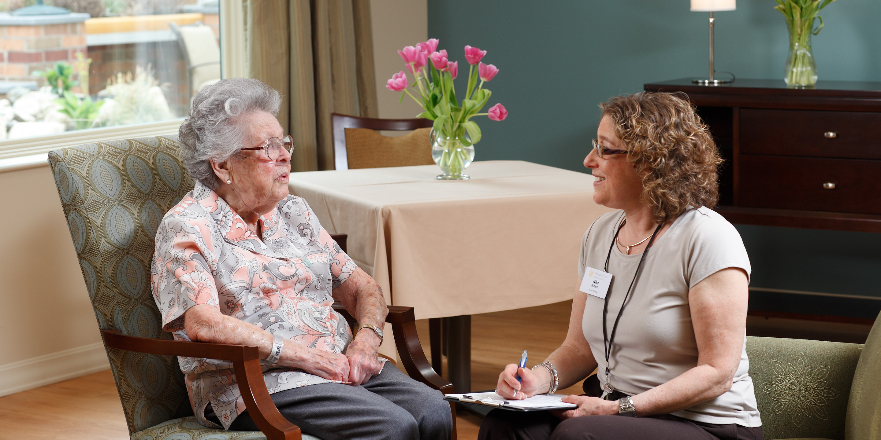 Senior woman in paisley shirt speaking with a woman holding a clipboard