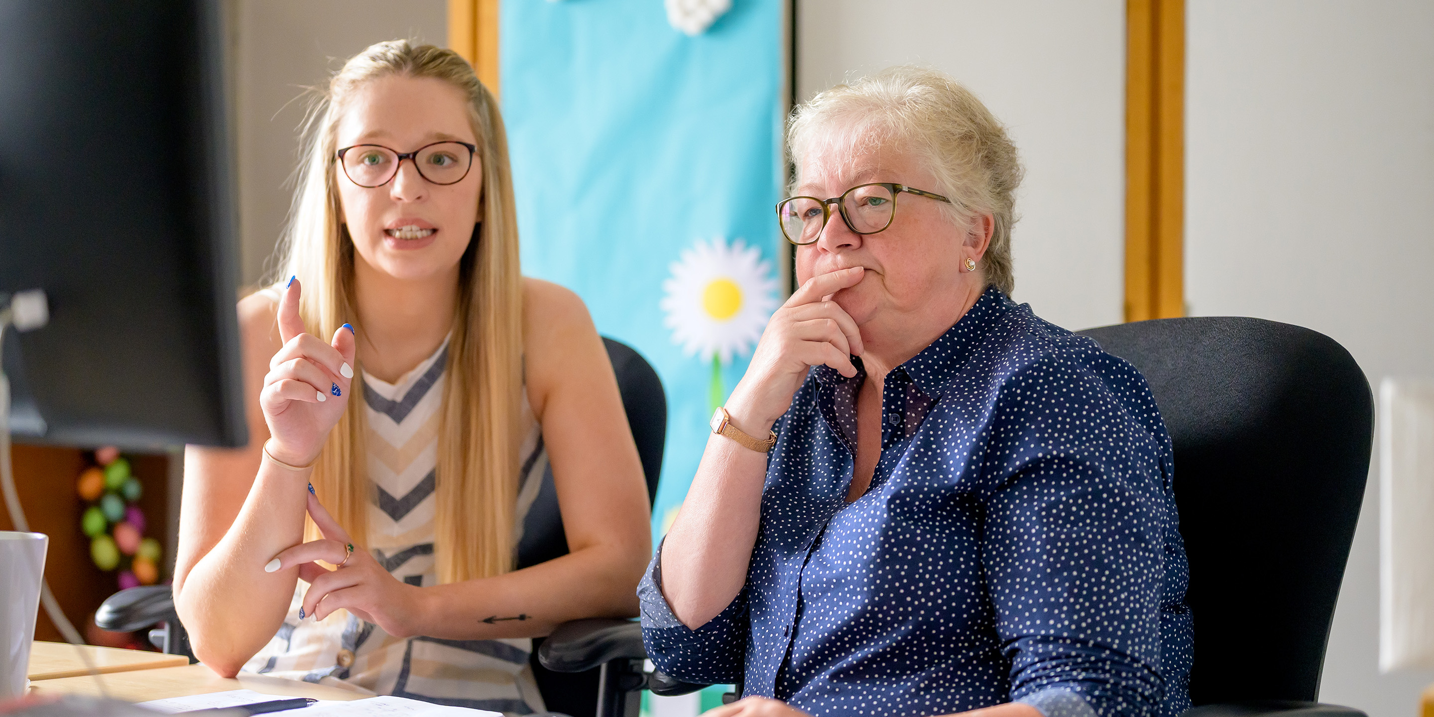 Younger woman and older woman sitting at desk discussing work