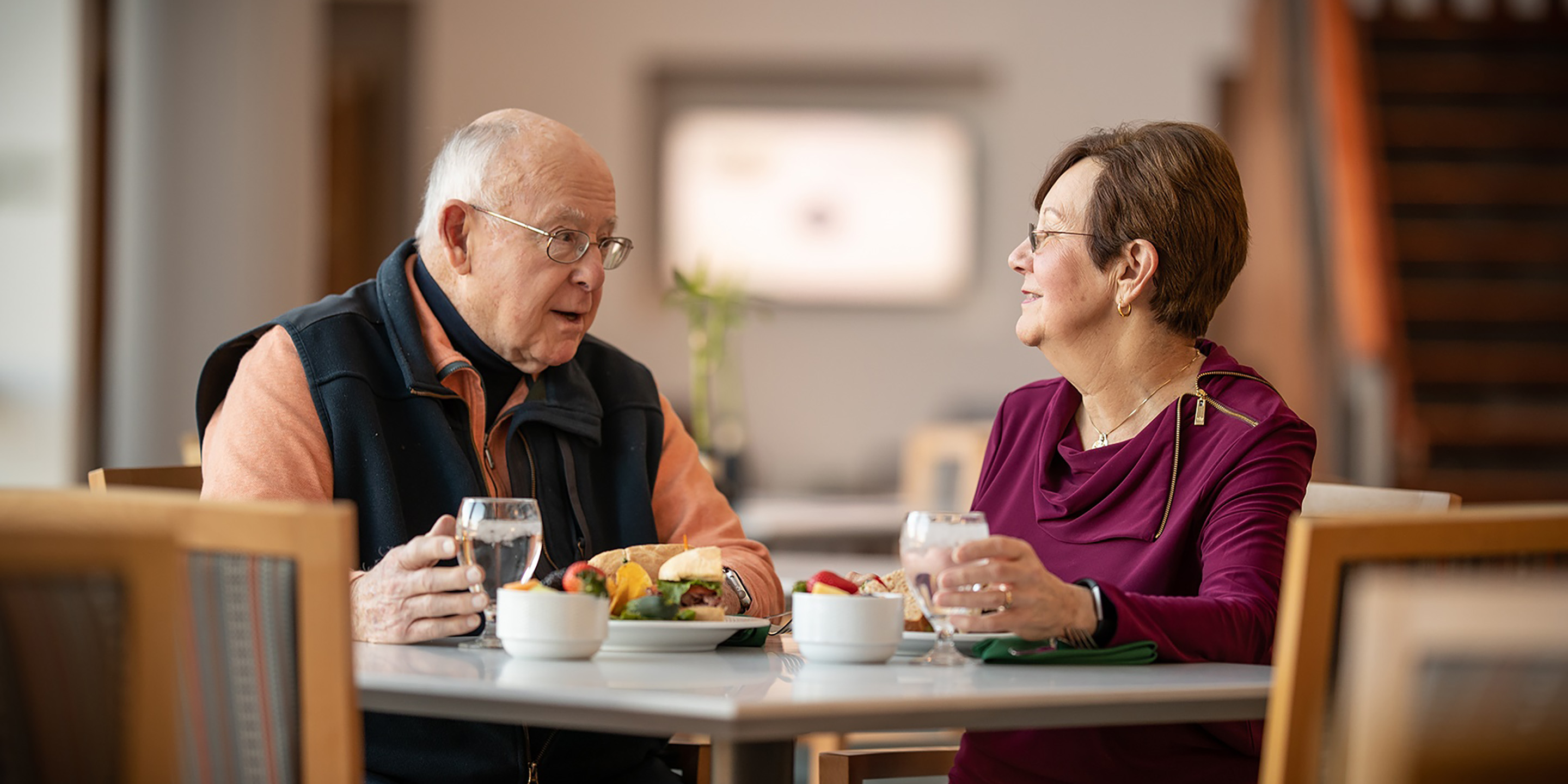 Two seniors sitting at a meal and holding glasses of water