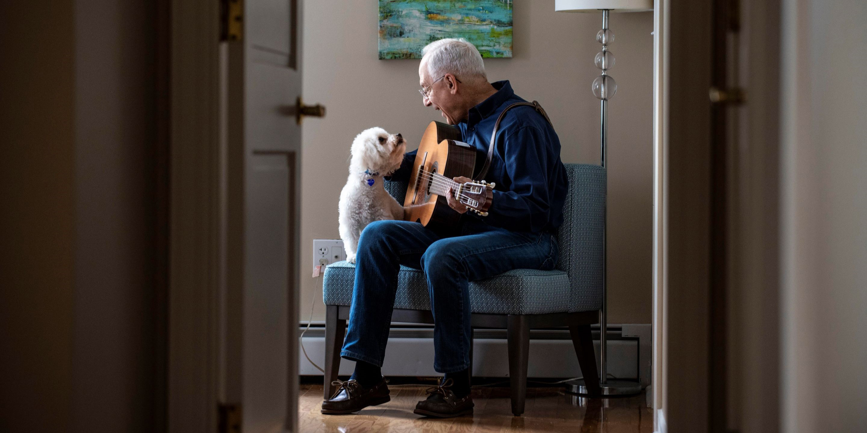 senior man sitting with dog playing guitar