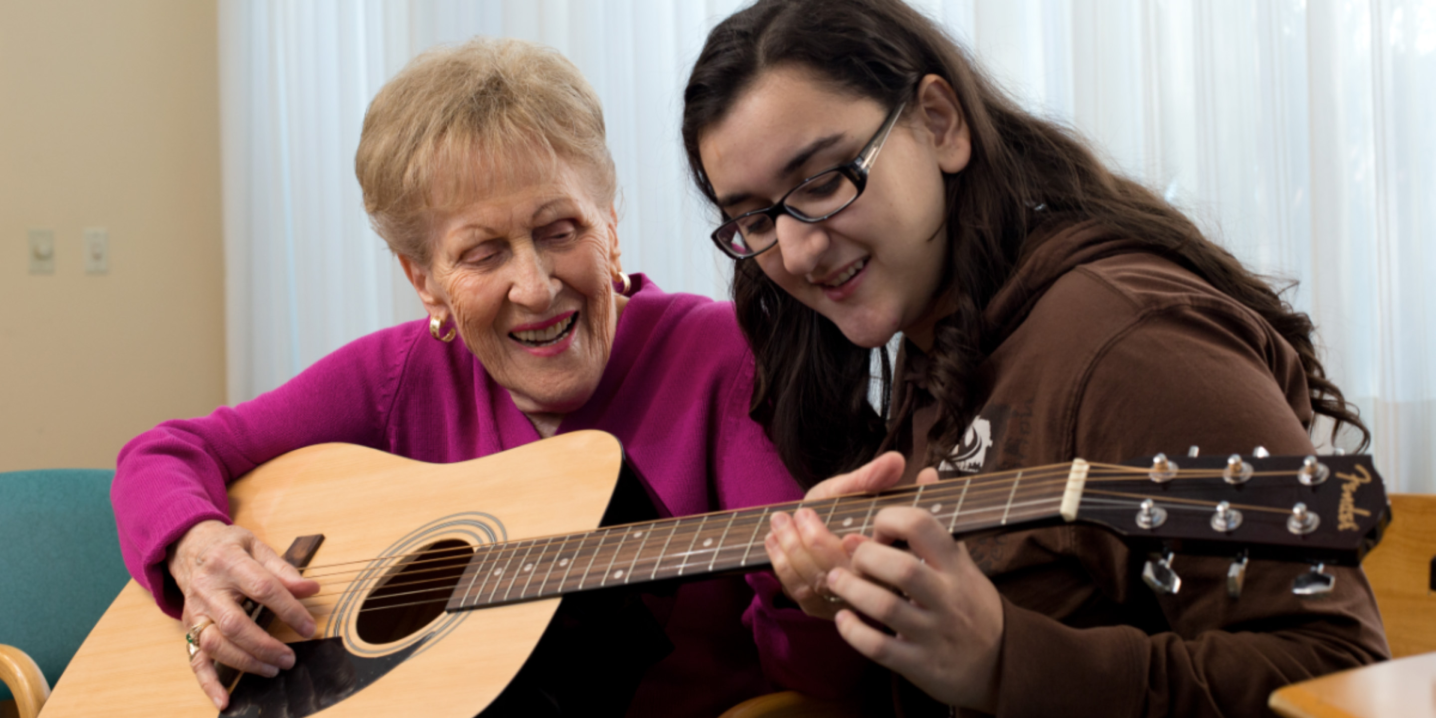 Young girl sitting with senior woman who is playing guitar