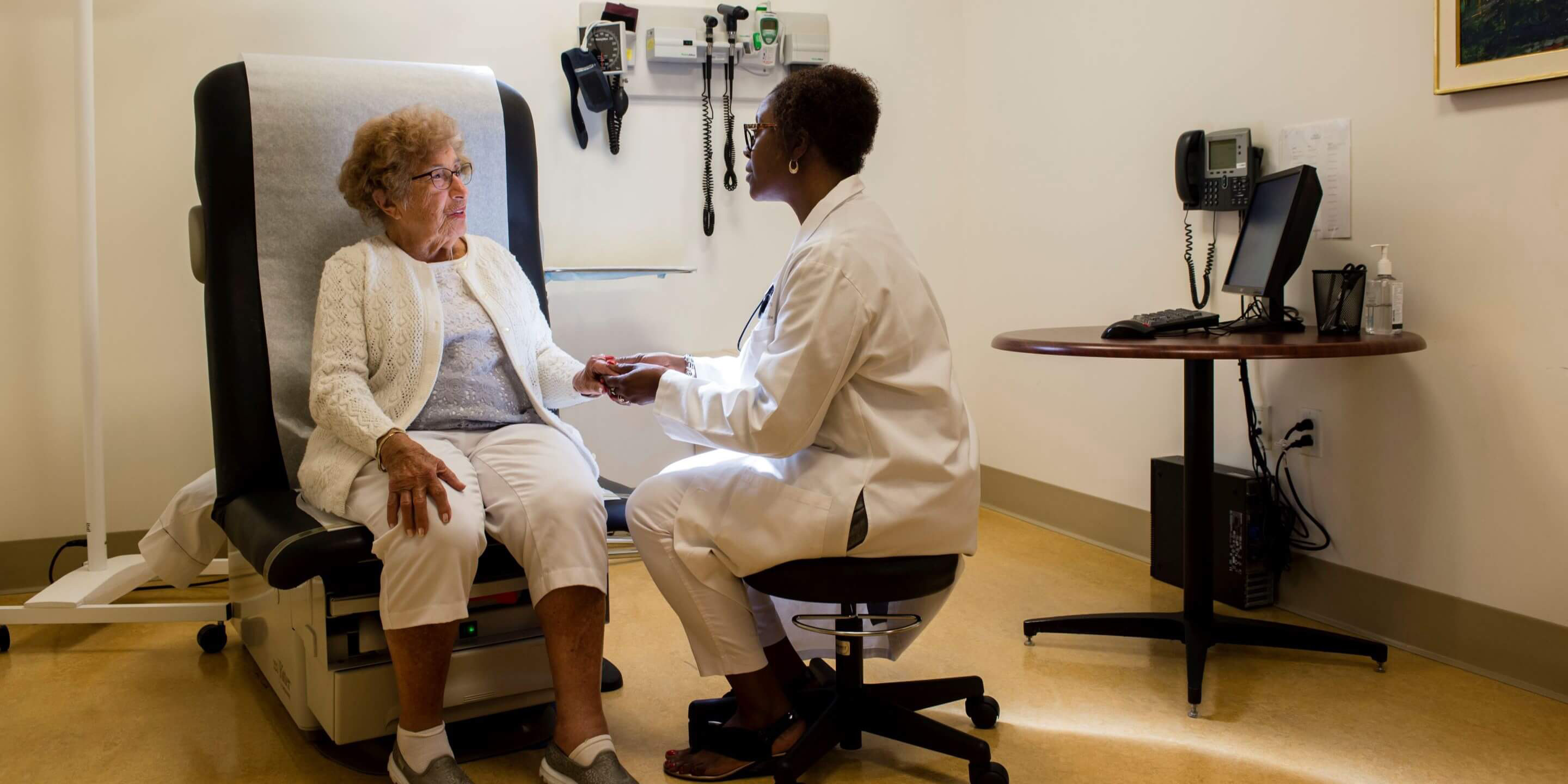 Older woman sitting in doctor office chair seeing a woman doctor