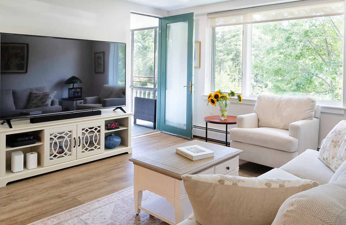 Living room with couch, sitting chair, flat screen tv, and a coffee table with a door opening to a balcony