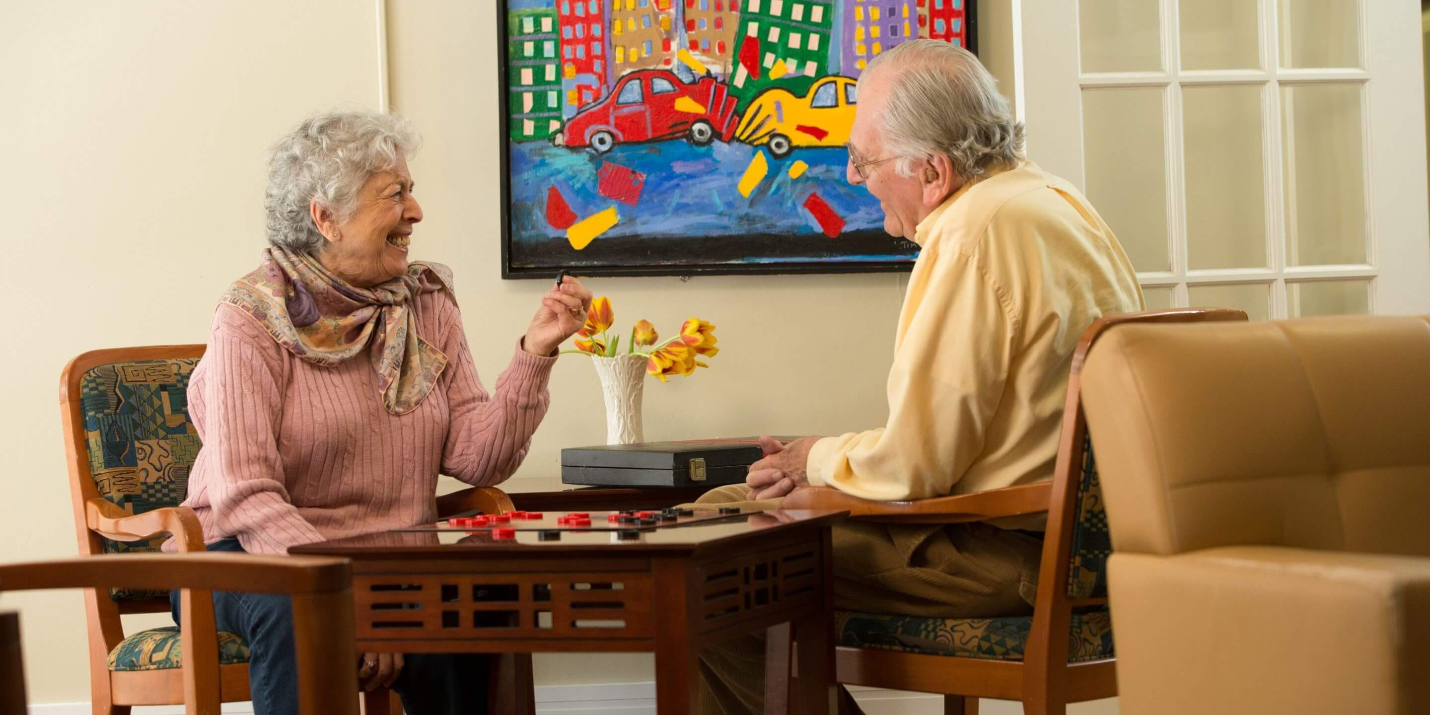 Older man and woman sitting at a table in a lounge area playing checkers.