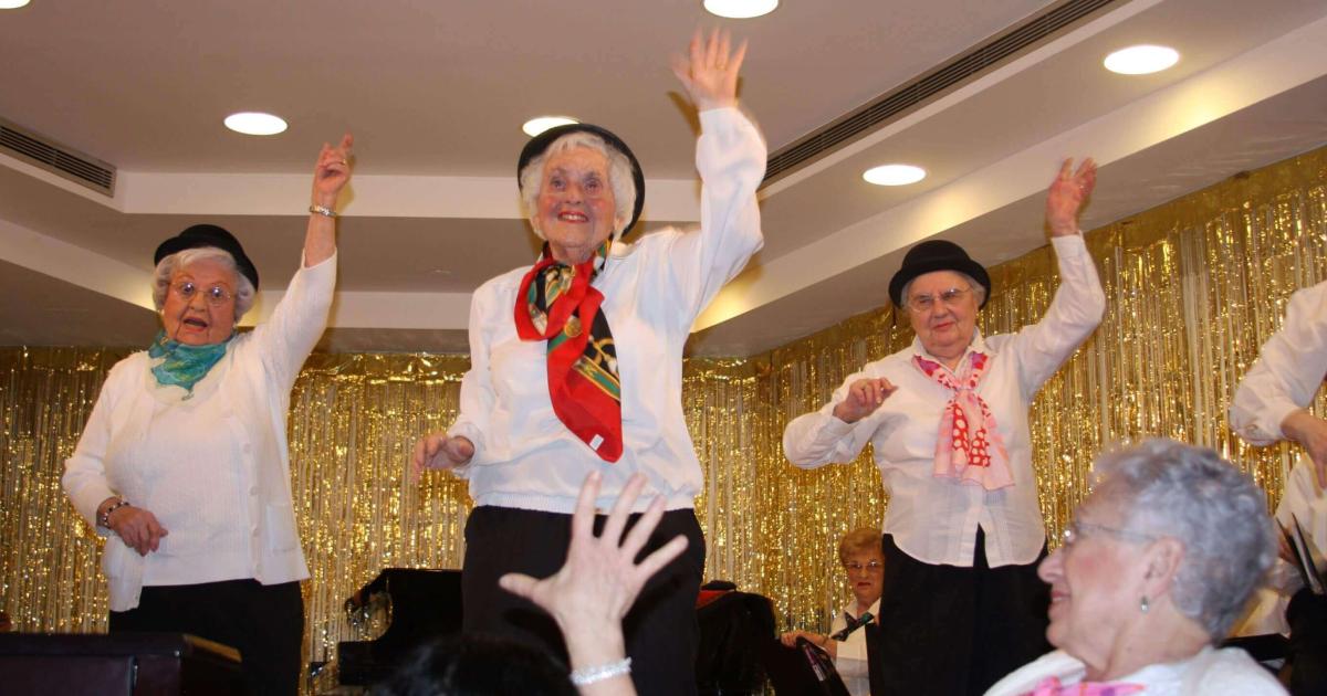 Older adults dancing together in a bright community room with an instructor leading them