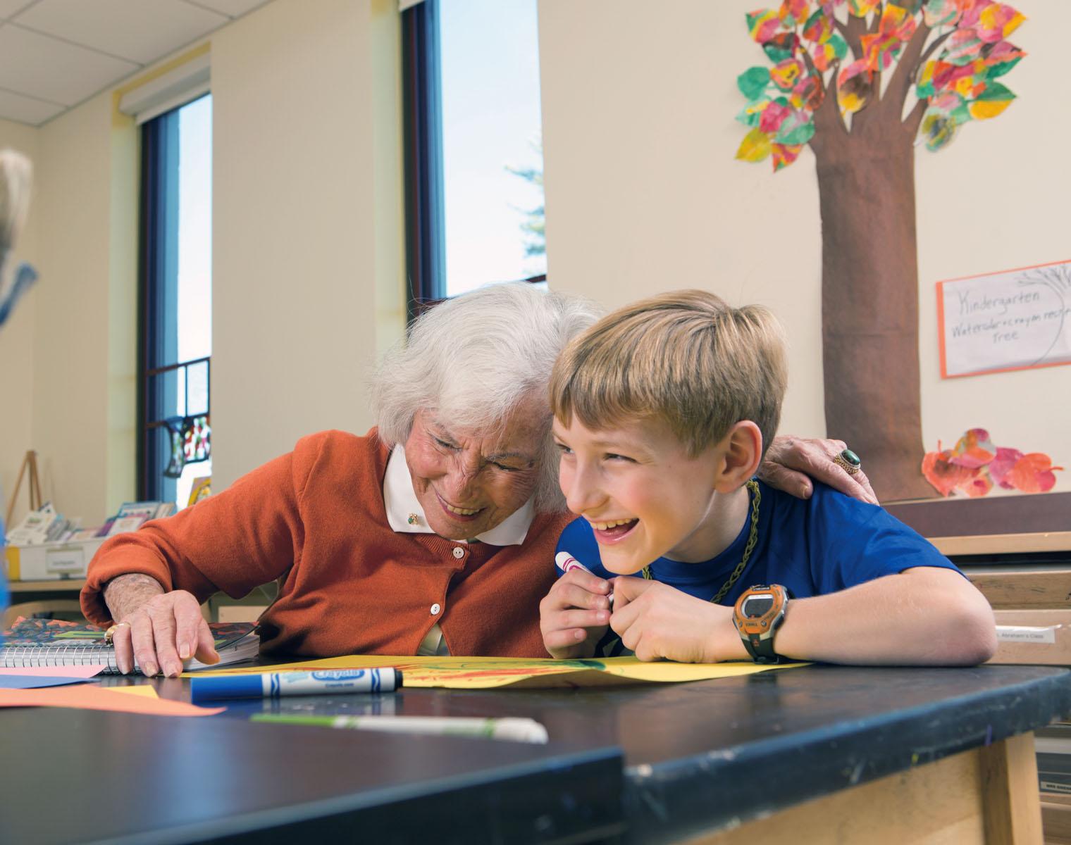 An older with and a school age boy laugh together while working on an art project.