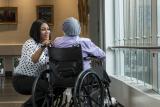 A female caregiver bends down to talk to a patient in a wheelchair 