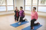 Two women residents do lunges on workout mats while one gets help from an instructor 