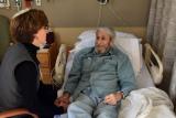 Rabbi Sara Paasche-Orlow sits and talks with a male patient while he lays in a hospital bed.