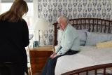 A Home Health worker stands and talks with a male patient while he sits in his bed.