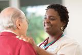 A young woman caregiver places her hands on an older man's shoulder. 