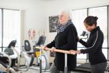 An older woman works out in a rehabilitation gym with a trainer