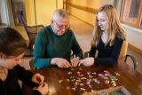 Two young girls sit with an elder man around a table and work on a puzzle together.