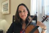 NewBridge on the Charles employee, Leticia Alvaraz, plays a violin while smiling 