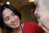 A female nurse in red scrubs sits and talks with a female resident 