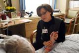 Rabbi Sara Paasche-Orlow  sits in a chair and holds a patients hand while talking to her 