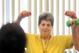 A female senior smiles and lifts dumbbells over her head in a fitness class 