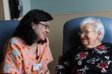 A smiling caregiver sits and talks with a senior 