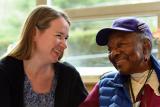 A Home Health worker smiles while sitting next to a smiling female senior 