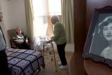 Hebrew SeniorLife's CEO Lou Woolf stands near a residents bed while talking to her and a female friend 